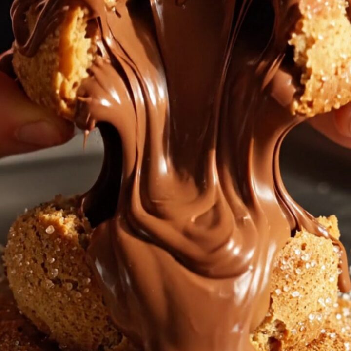 A close-up of a warm churro cookie being broken open to reveal a flowing dulce de leche center.
