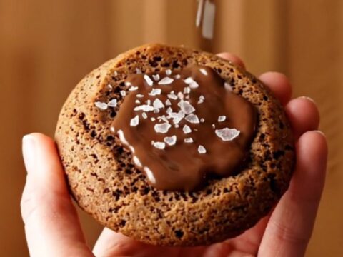 A close-up of a warm brown butter espresso cookie being pulled apart, showing melted chocolate inside.