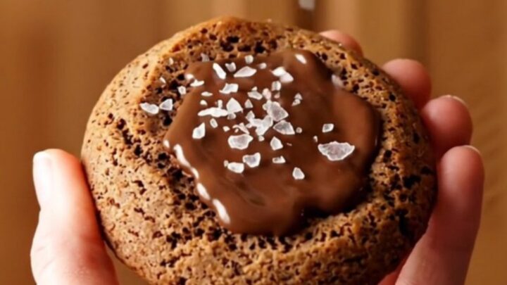 A close-up of a warm brown butter espresso cookie being pulled apart, showing melted chocolate inside.
