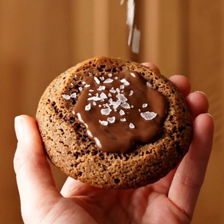 A close-up of a warm brown butter espresso cookie being pulled apart, showing melted chocolate inside.