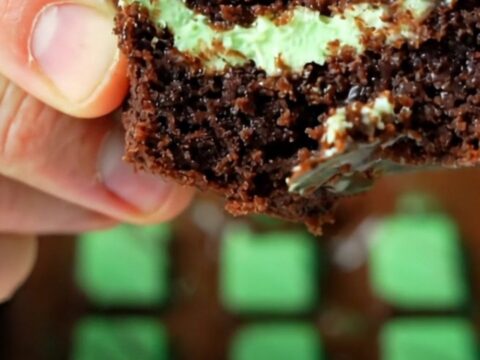 Extreme close-up of a warm knife slicing through a fudgy dark brownie with a glossy green-swirled Andes mint glaze.