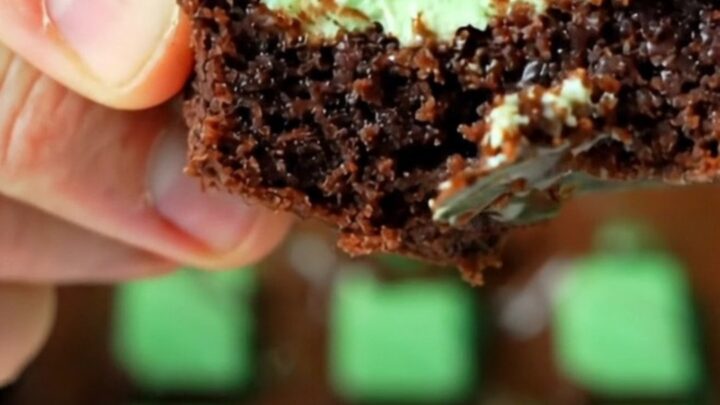 Extreme close-up of a warm knife slicing through a fudgy dark brownie with a glossy green-swirled Andes mint glaze.