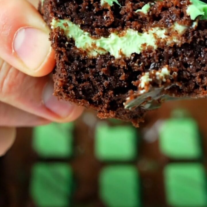 Extreme close-up of a warm knife slicing through a fudgy dark brownie with a glossy green-swirled Andes mint glaze.