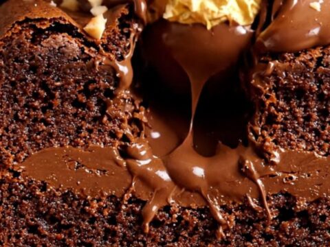 A close-up shot of a Ferrero Rocher stuffed brownie sliced in half, revealing the hazelnut truffle and molten Nutella center.