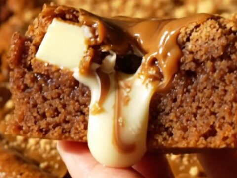 A close-up shot of a thick, golden-brown blondie square with visible white chocolate chunks and a swirl of Biscoff cookie