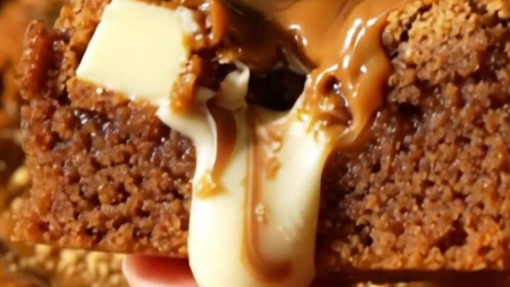 A close-up shot of a thick, golden-brown blondie square with visible white chocolate chunks and a swirl of Biscoff cookie