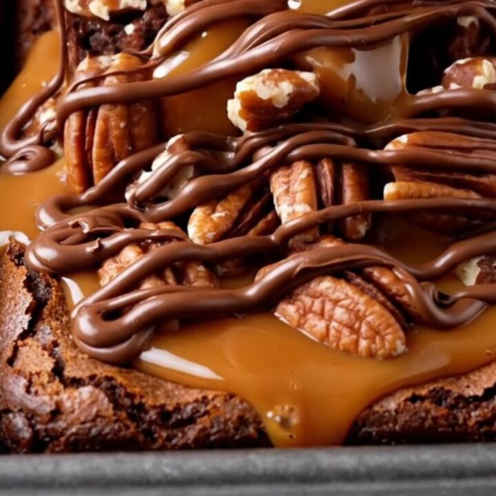 Extreme close-up of a turtle brownie being pulled apart, showing a thick layer of stretchy salted caramel and toasted pecans.