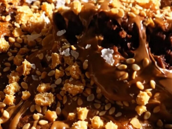A close-up of a fudgy brownie square with swirls of creamy tahini and a golden, flaky halva topping.