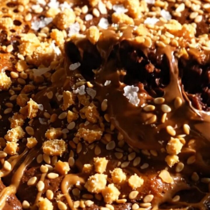 A close-up of a fudgy brownie square with swirls of creamy tahini and a golden, flaky halva topping.