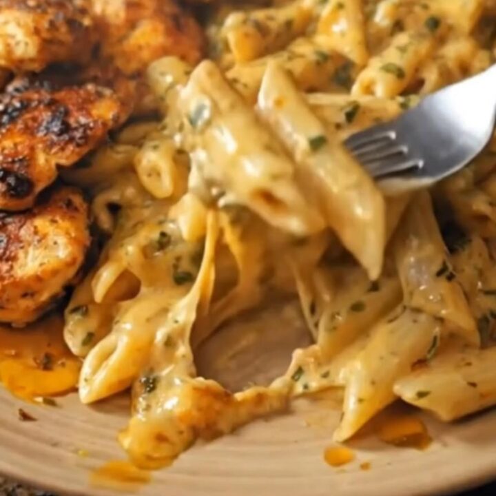 A plated serving of sliced Cajun chicken breast resting next to creamy Cajun Alfredo penne pasta