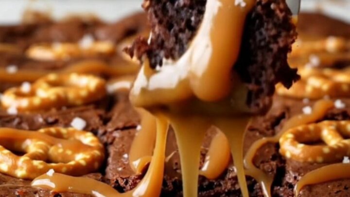 A top-down view of a square pan filled with dark, fudgy brownies topped with swirling ribbons of caramel and mini pretzel