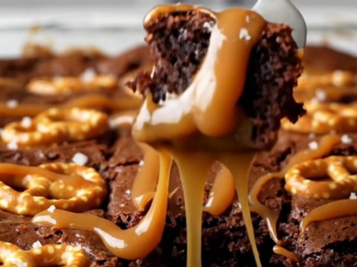 A top-down view of a square pan filled with dark, fudgy brownies topped with swirling ribbons of caramel and mini pretzel