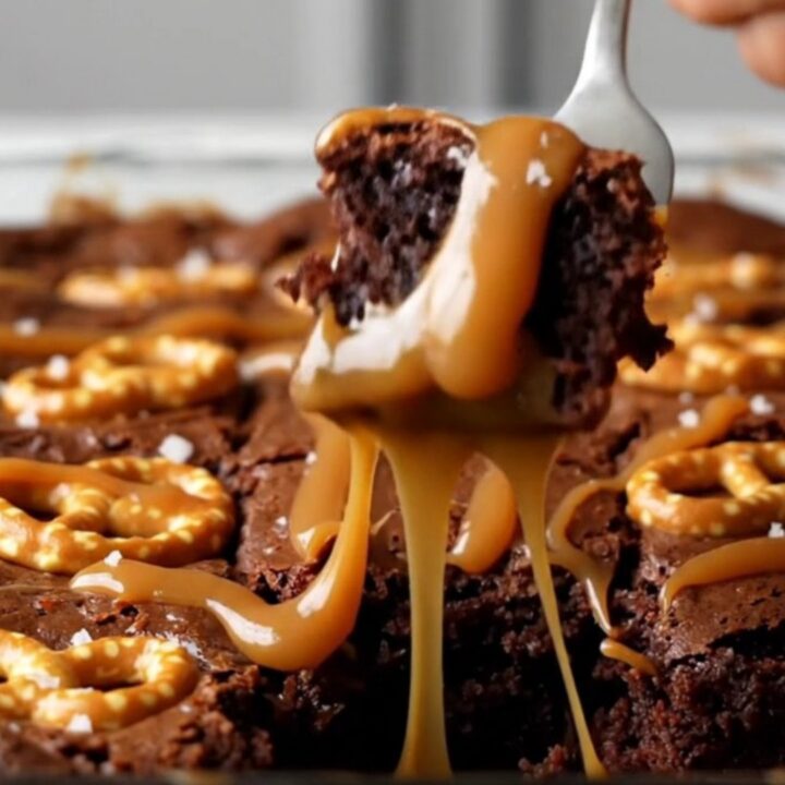 A top-down view of a square pan filled with dark, fudgy brownies topped with swirling ribbons of caramel and mini pretzel