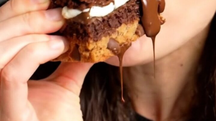 A tall, square slice of a triple-layer brookie bar showing distinct layers of cookie dough, Oreos, and fudge brownie.