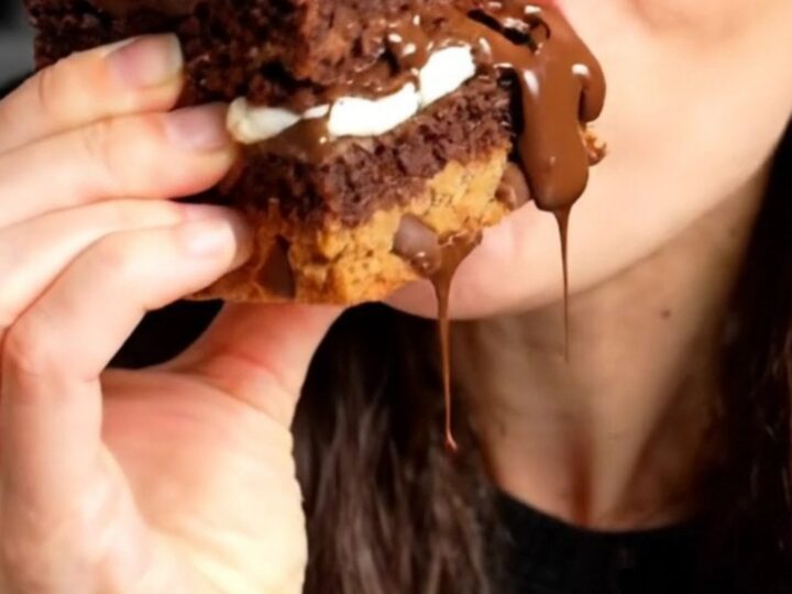 A tall, square slice of a triple-layer brookie bar showing distinct layers of cookie dough, Oreos, and fudge brownie.