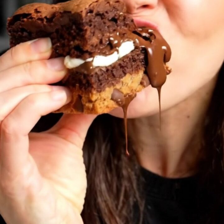 A tall, square slice of a triple-layer brookie bar showing distinct layers of cookie dough, Oreos, and fudge brownie.