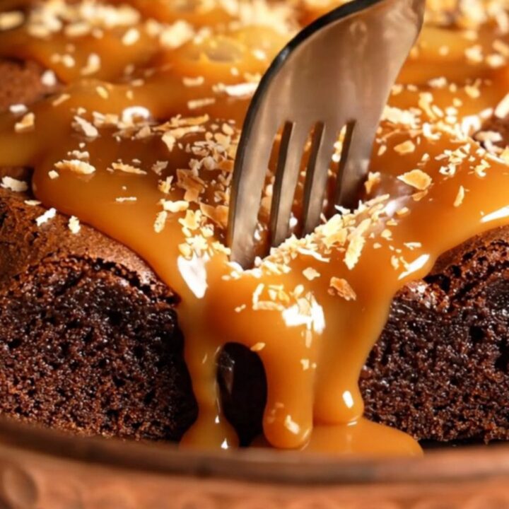 Extreme close-up of a dense dark chocolate brownie being pulled apart to reveal caramel swirls.