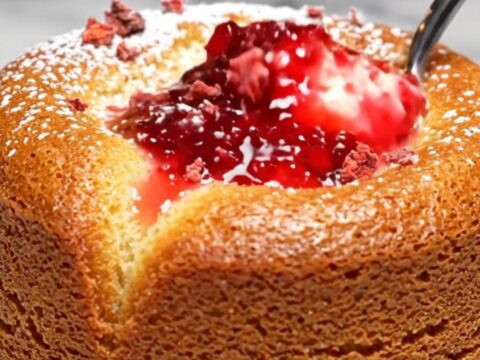 A close-up of a white chocolate lava cake with a vibrant pink raspberry coulis center spilling out onto a plate.