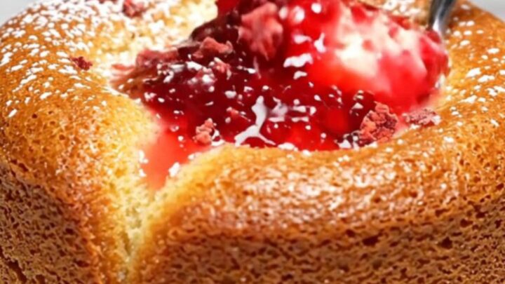 A close-up of a white chocolate lava cake with a vibrant pink raspberry coulis center spilling out onto a plate.