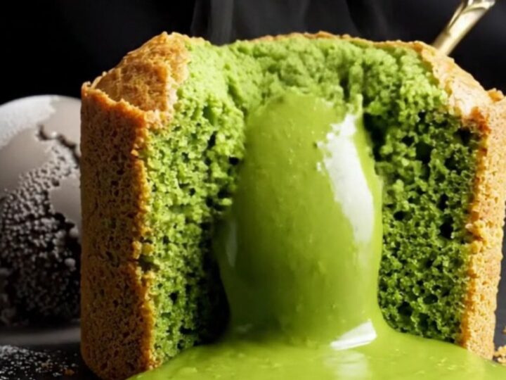 A close-up shot of a jade-green matcha molten lava cake with a flowing liquid center on a black stone table.