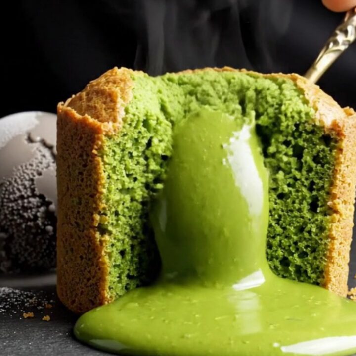 A close-up shot of a jade-green matcha molten lava cake with a flowing liquid center on a black stone table.