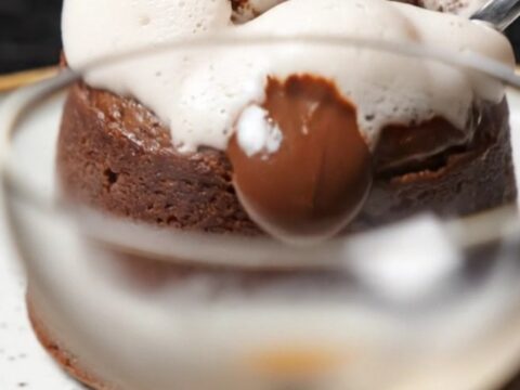 A close-up of a spoon breaking into a dark, glossy molten lava cake with a warm chocolate and espresso center.