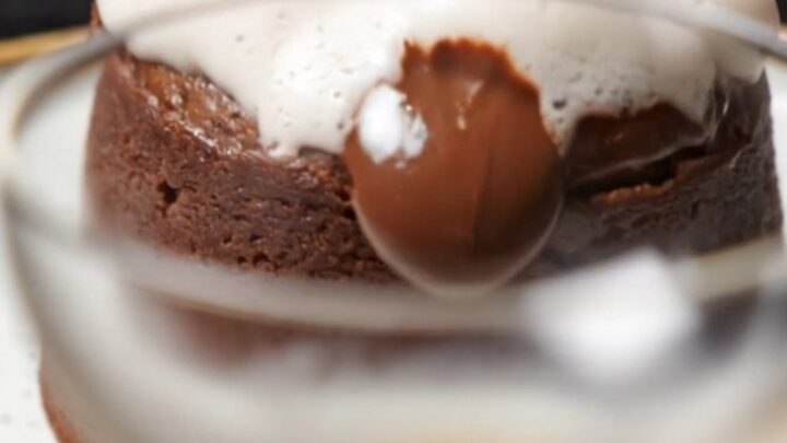 A close-up of a spoon breaking into a dark, glossy molten lava cake with a warm chocolate and espresso center.