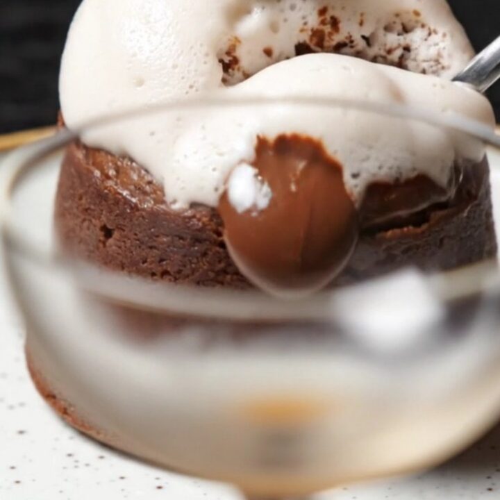 A close-up of a spoon breaking into a dark, glossy molten lava cake with a warm chocolate and espresso center.