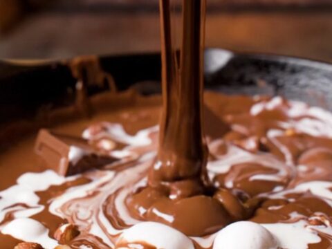 A cast-iron skillet filled with a molten triple chocolate fondue with marshmallow swirls and hazelnuts.