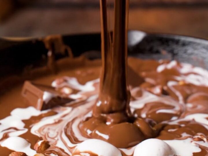 A cast-iron skillet filled with a molten triple chocolate fondue with marshmallow swirls and hazelnuts.