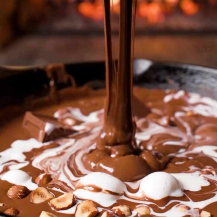 A cast-iron skillet filled with a molten triple chocolate fondue with marshmallow swirls and hazelnuts.