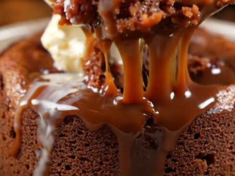 A close-up of dark chocolate toffee sauce being poured over a warm, spongy date and chocolate pudding cake.