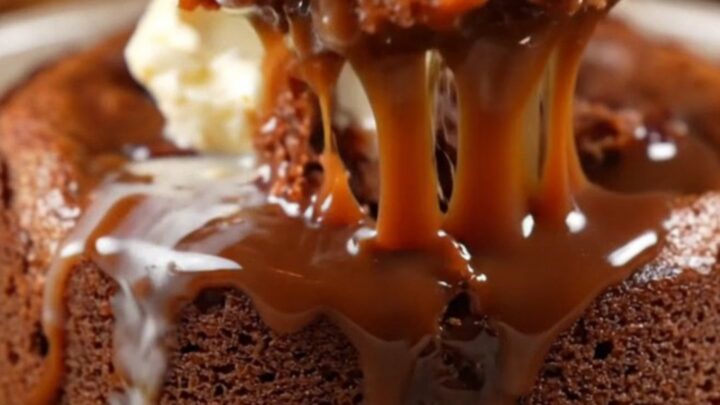 A close-up of dark chocolate toffee sauce being poured over a warm, spongy date and chocolate pudding cake.
