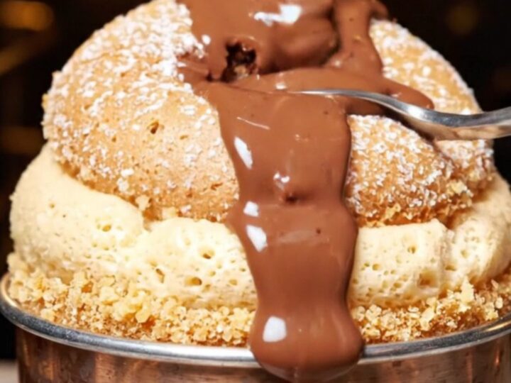 A tall, airy dark chocolate souffle in a ramekin with steam rising, topped with fresh orange zest.