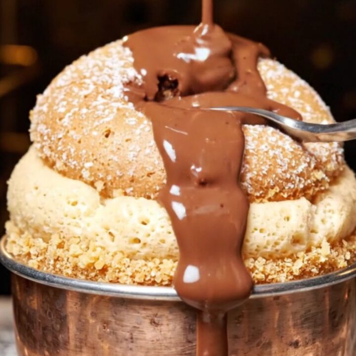 A tall, airy dark chocolate souffle in a ramekin with steam rising, topped with fresh orange zest.