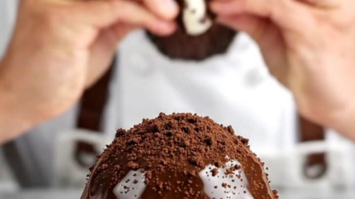 A close-up view of a dark chocolate-covered Oreo truffle broken in half, showing the creamy black and white interior.