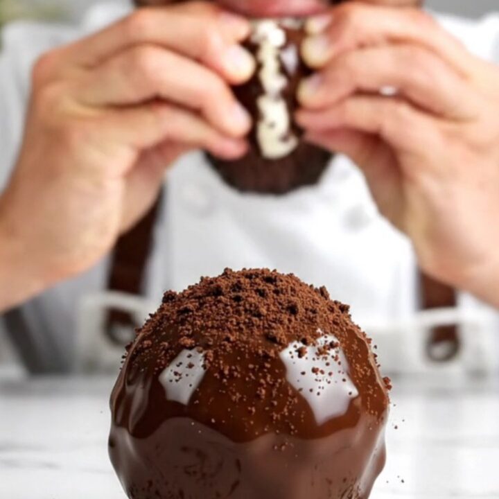 A close-up view of a dark chocolate-covered Oreo truffle broken in half, showing the creamy black and white interior.