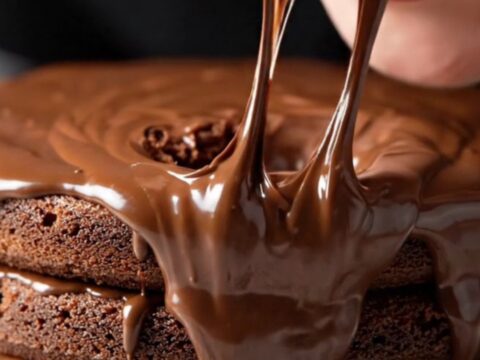 A towering three-layer chocolate cake with glossy fudge frosting and a fork sinking into it.