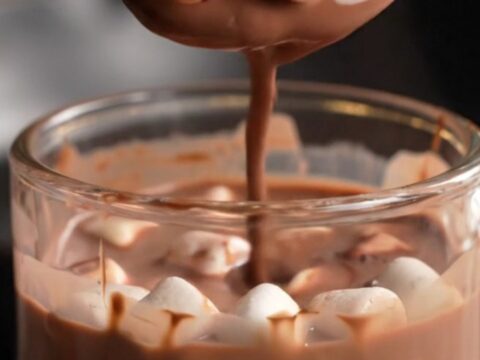 A glossy dark chocolate sphere in a glass mug being covered by steaming hot milk.
