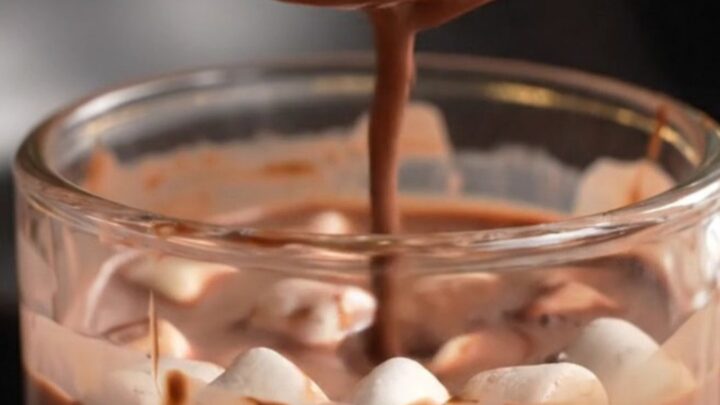 A glossy dark chocolate sphere in a glass mug being covered by steaming hot milk.
