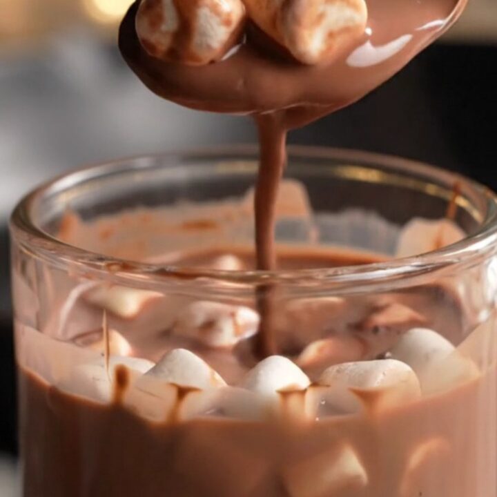 A glossy dark chocolate sphere in a glass mug being covered by steaming hot milk.