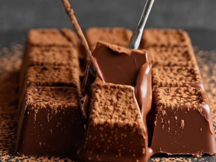 A close-up of a warm knife slicing through a velvety block of dark chocolate dusted with cocoa powder.
