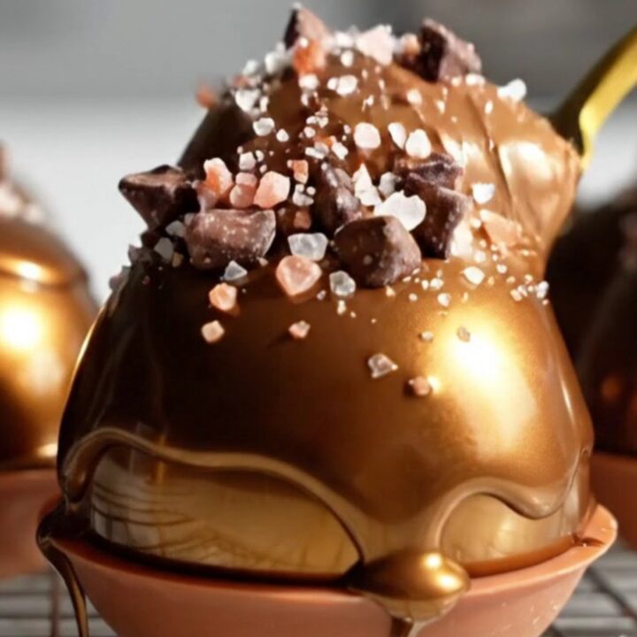 A close-up shot of a gold spoon scooping into a glossy, dark chocolate mousse dome.