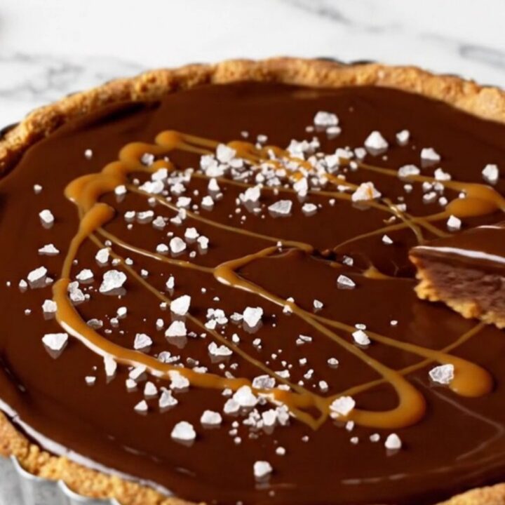 A close-up view of a no-bake dark chocolate ganache tart with a Biscoff crust, garnished with sea salt and caramel.