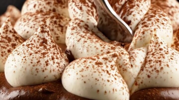 A close-up of a slice of tiramisu tart showing distinct layers of chocolate crust, ladyfingers, ganache, and mascarpone.