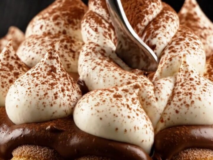 A close-up of a slice of tiramisu tart showing distinct layers of chocolate crust, ladyfingers, ganache, and mascarpone.