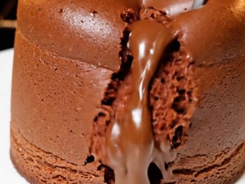 A tall, jiggly chocolate souffle cheesecake with a glossy top on a white plate.