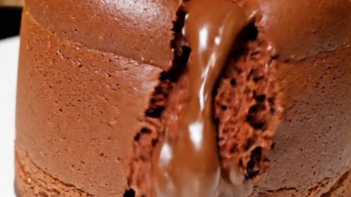 A tall, jiggly chocolate souffle cheesecake with a glossy top on a white plate.