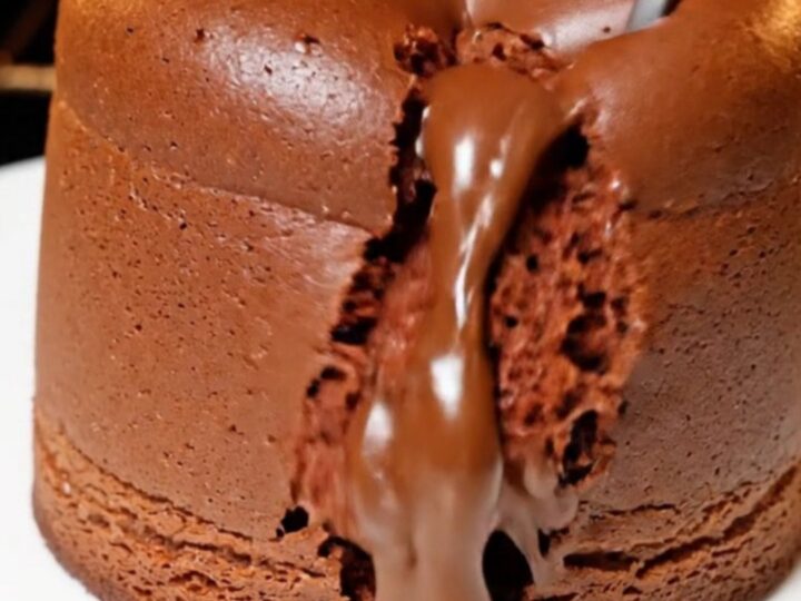 A tall, jiggly chocolate souffle cheesecake with a glossy top on a white plate.
