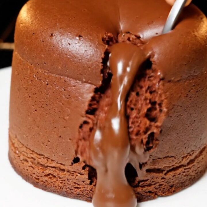 A tall, jiggly chocolate souffle cheesecake with a glossy top on a white plate.
